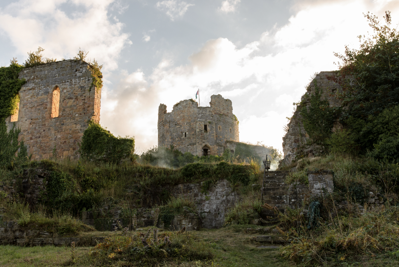 A view of a broken castle like building sitting at the top of a hill, with stairs leading up the hill on the right hand side.
